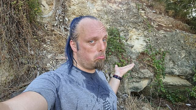 Dan, dripping with sweat, stands half-way up a cliff face.