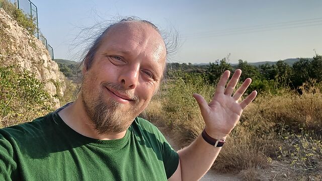 Dan, a white man in a green shirt, waves to the camera from a rural Spanish trail.
