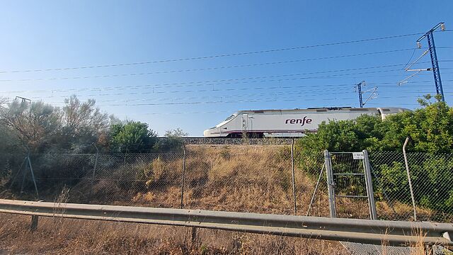 A 'renfe' high speed passenger train rockets along a track atop a raised embankment.