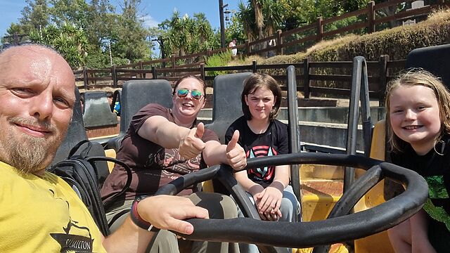 A man (Dan), a woman (Ruth), and two children sit in a circular boat on a 'river rapids' style ride.