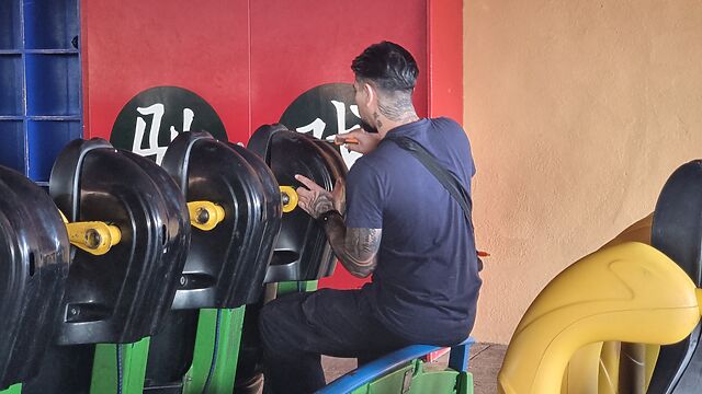 A man with a screwdriver repairs the restraint system on a rollercoaster car.
