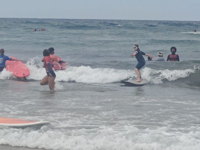 A group of children in wetsuits surf on low waves.