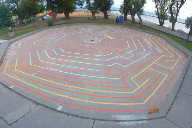 A large octagonal labyrinth drawn in a dry paddling pool in a park.