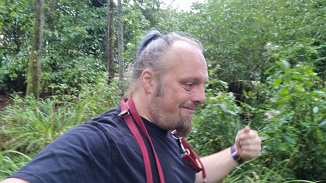 Dan stomps through thick undergrowth, a dog's lead hanging around his shoulders.