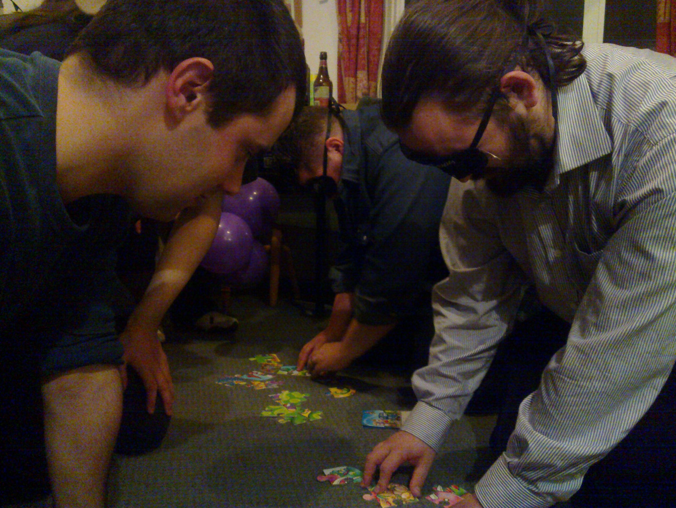 Full image of Alec and JTA, blindfolded, attempt to solve jigsaws.