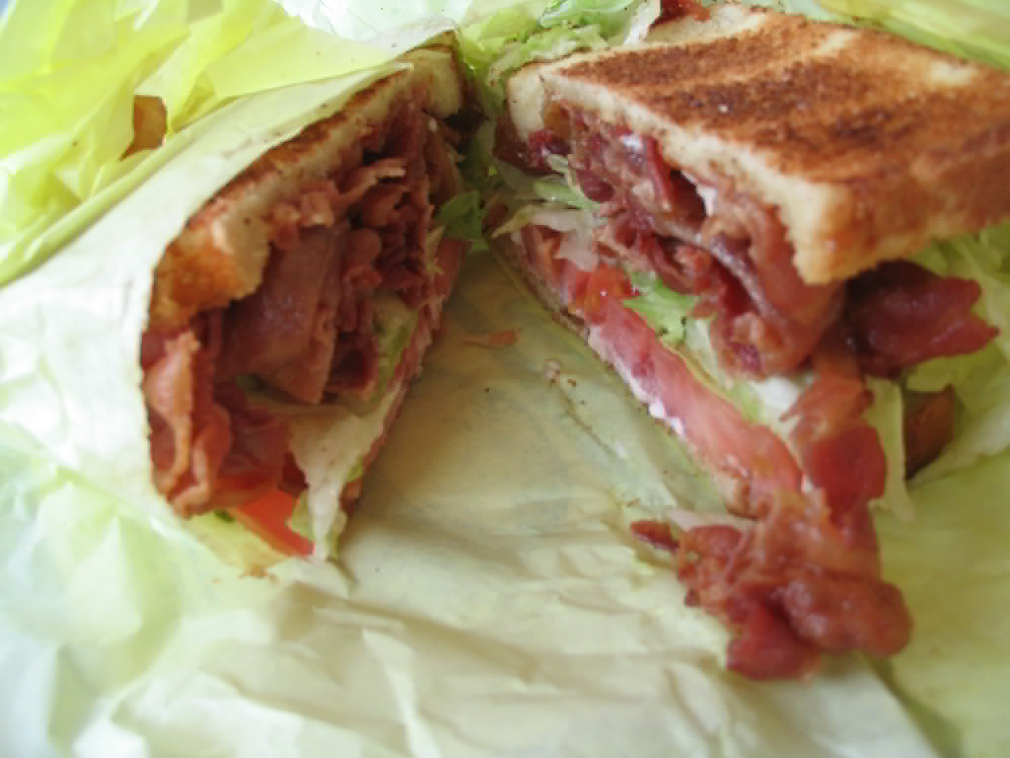 Larger image: a thick, delicious-looking BLT sandwich on toasted bread, wrapped in paper and sliced down the middle.