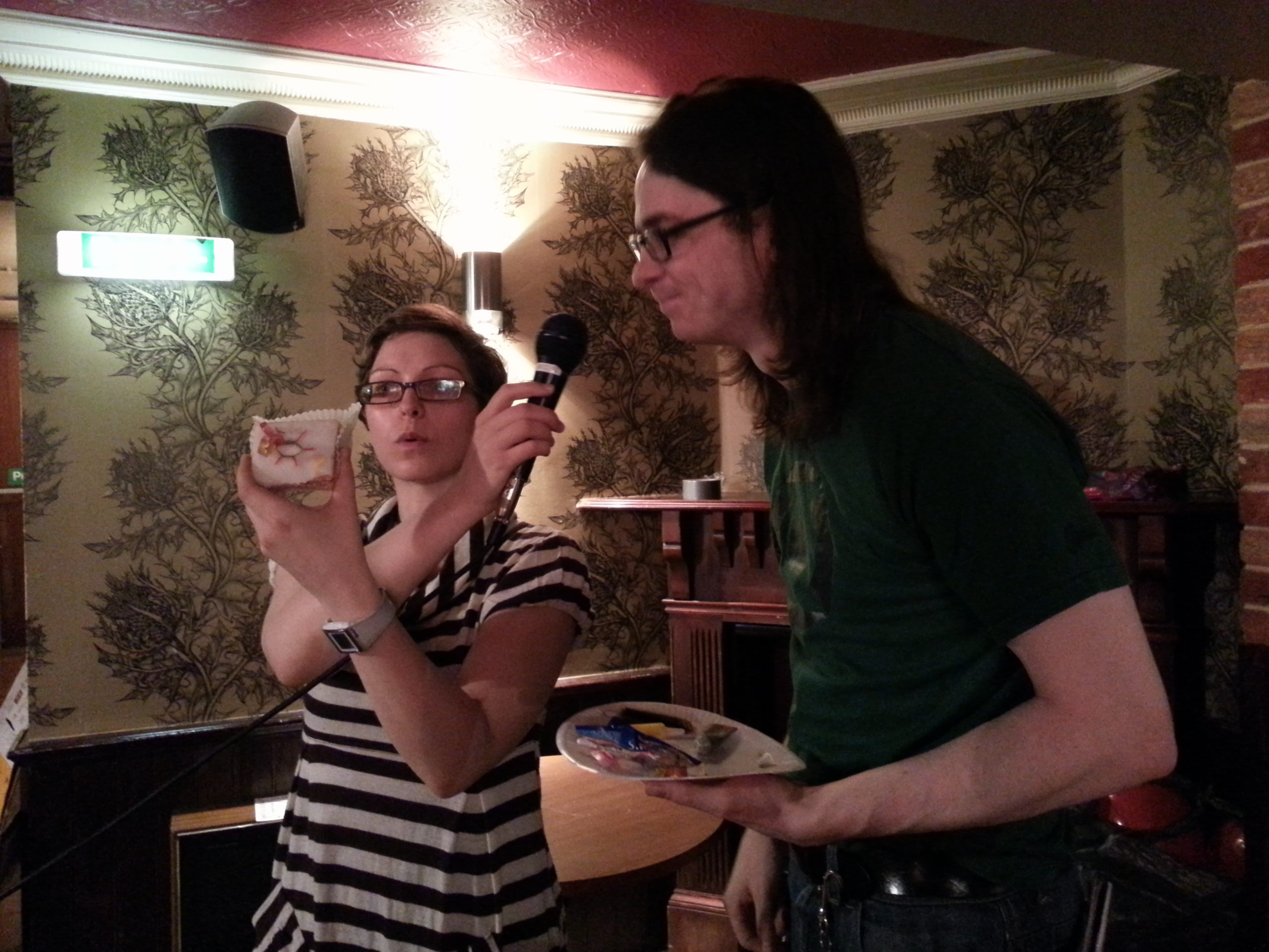 Full image of Matt R with Helen Arney of Domestic Science, explaining why he's drawn a silicon lattice onto an iced bun.