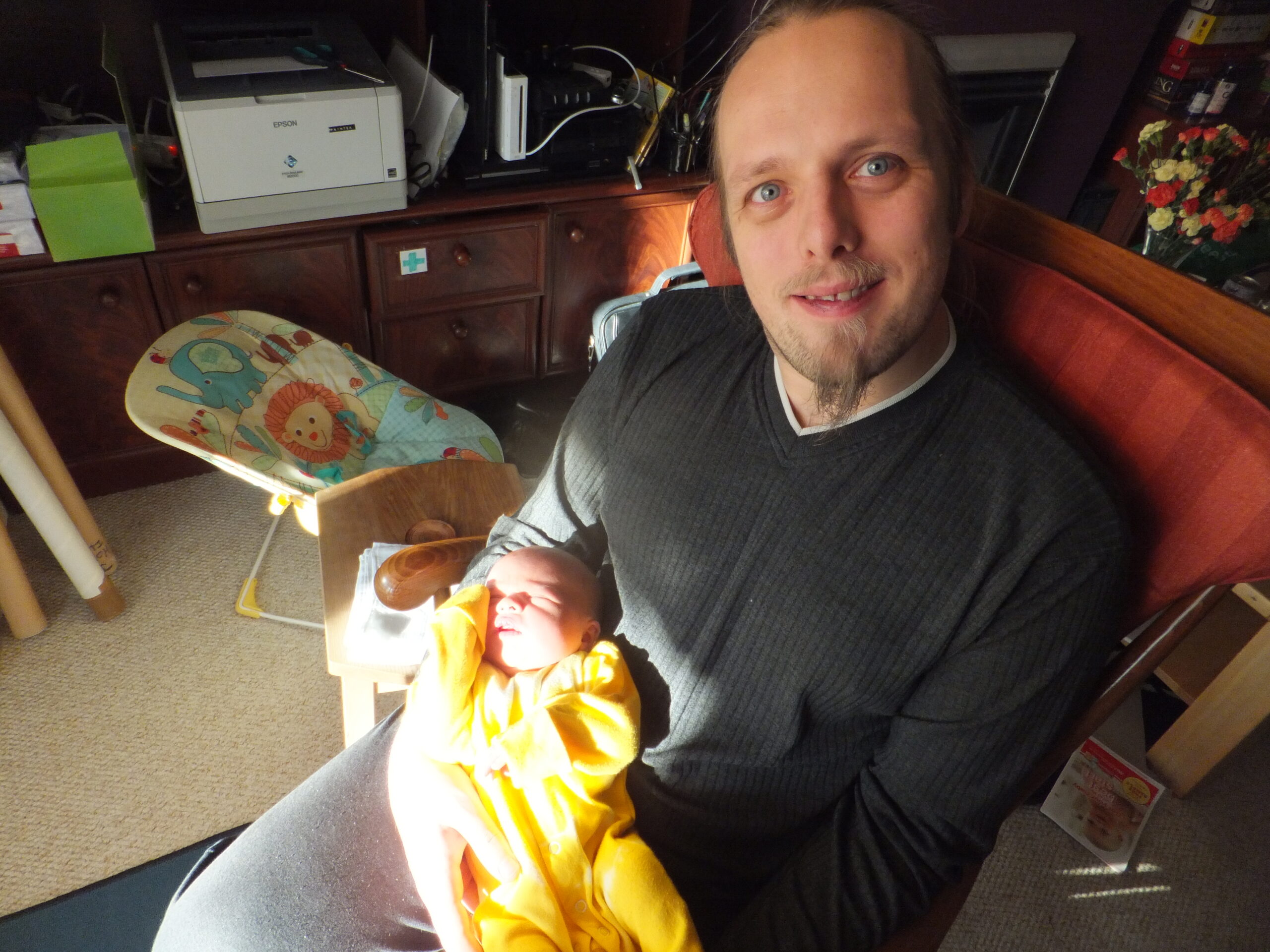 Full image of Dan, sitting in the sunlight, rocking the baby.