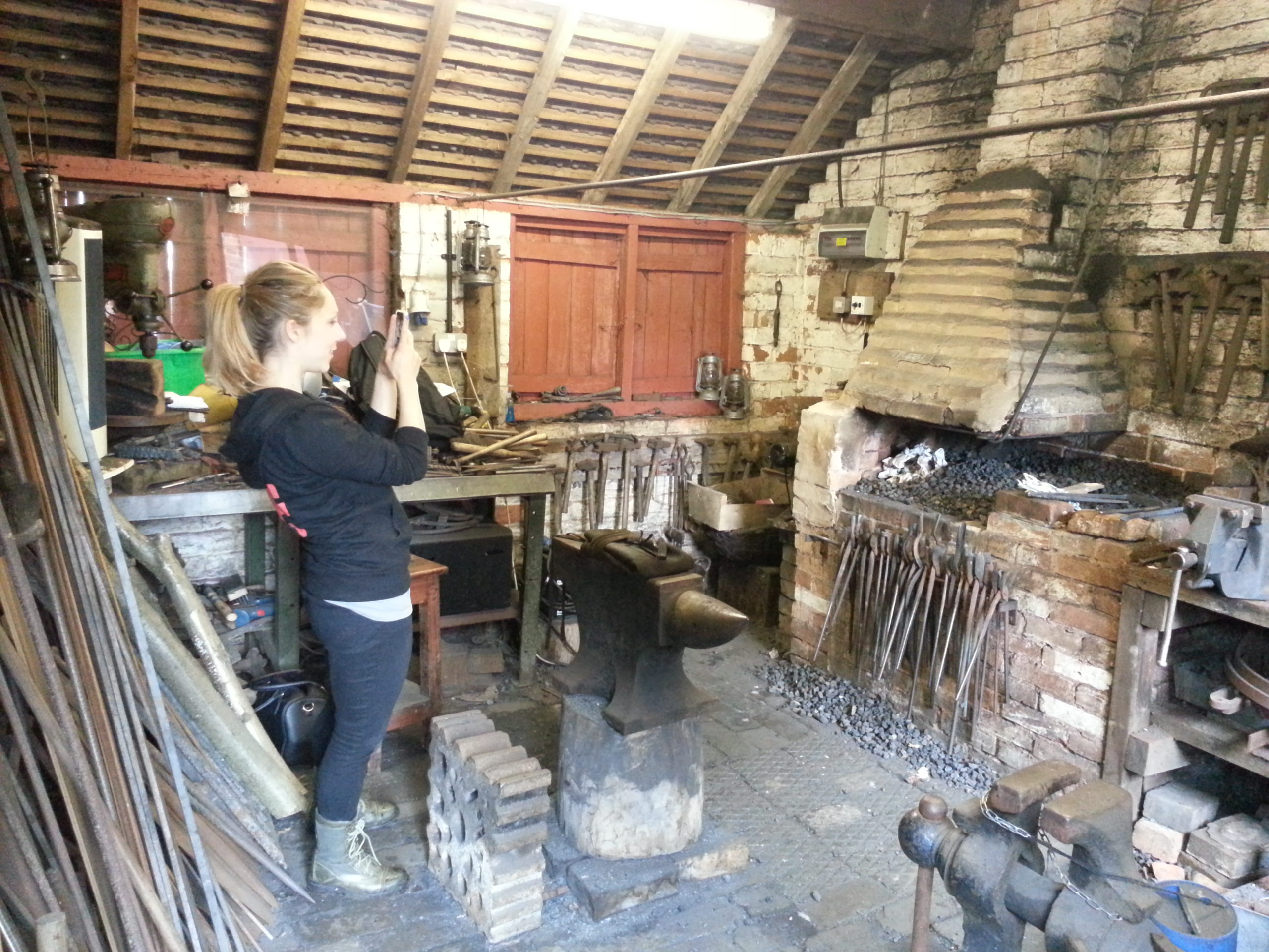 Full image of Liz leans back to try to fit as much of the forge as possible into the viewfinder.