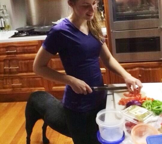 Woman cutting vegetables with dog behind; from this angle, she looks like a centaur.
