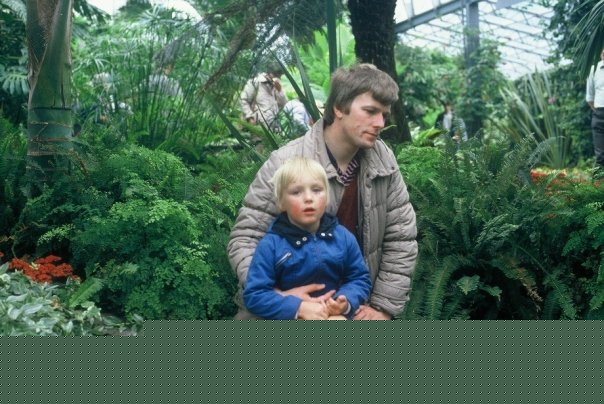 Full image of Dan sits on his father's knee. 1980s.