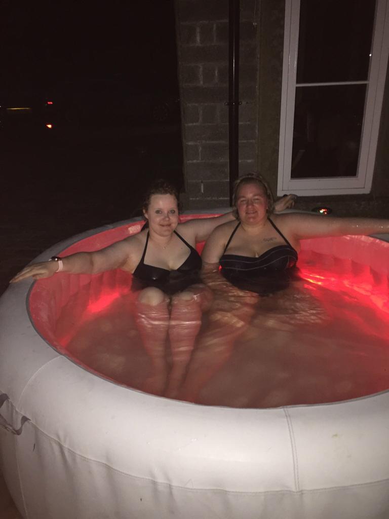 Full image of Jemma and Becky in the hot tub, in the dark.