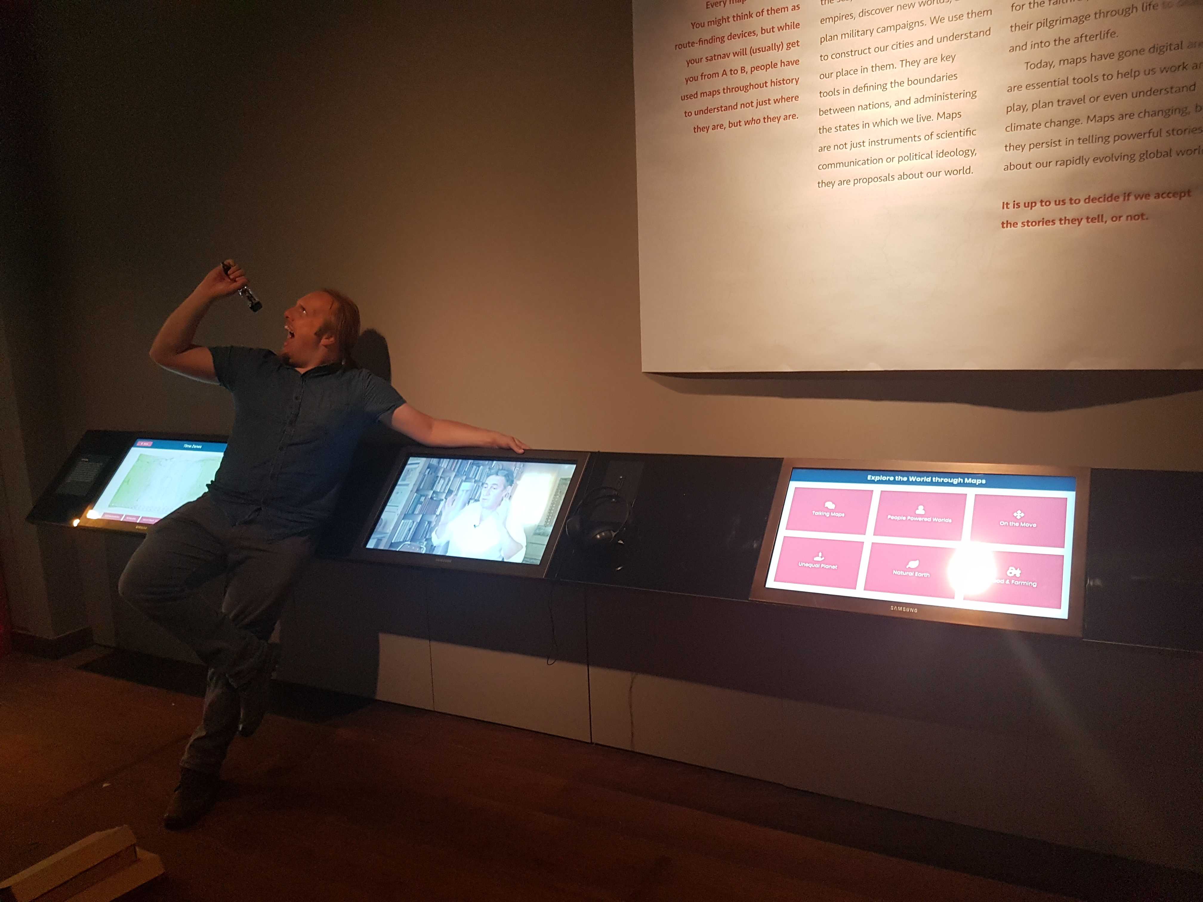 Full image of Dan sings into a screwdriver handle alongside three touchscreens.
