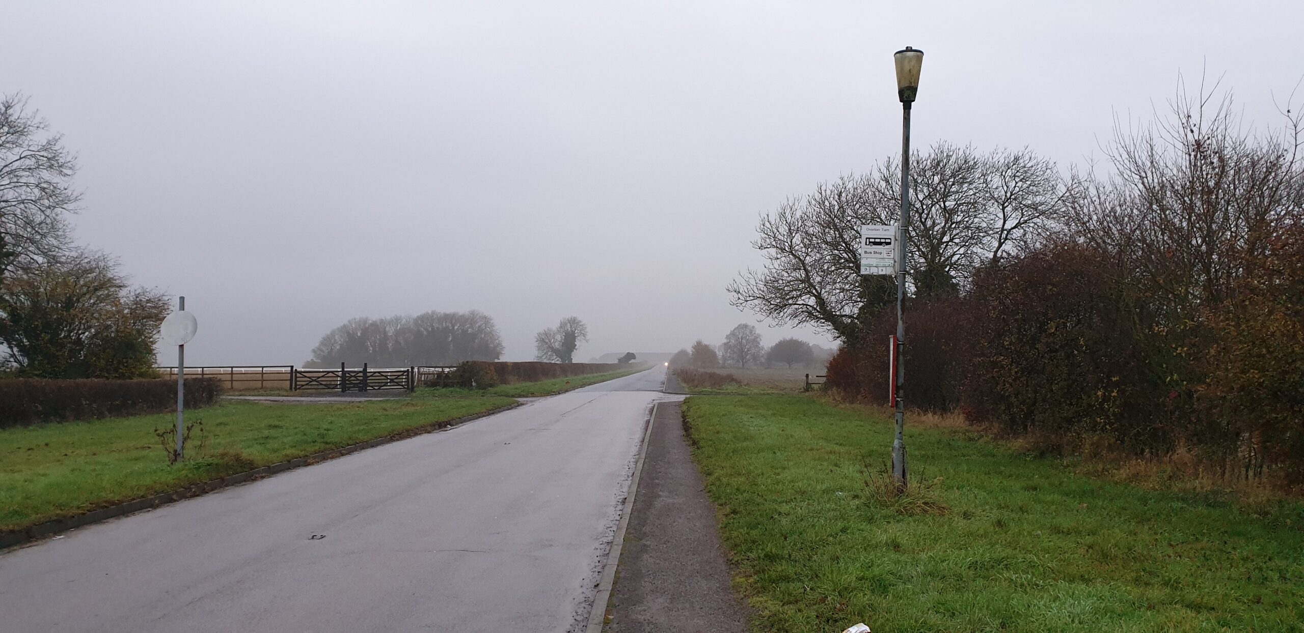 Full image of Bus stop attached to a lamppost on a misty, empty road.