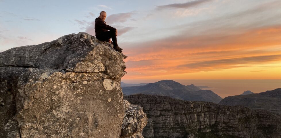 Dan sitting on a rock on Table Mountain, Cape Town, with a sunset in the background