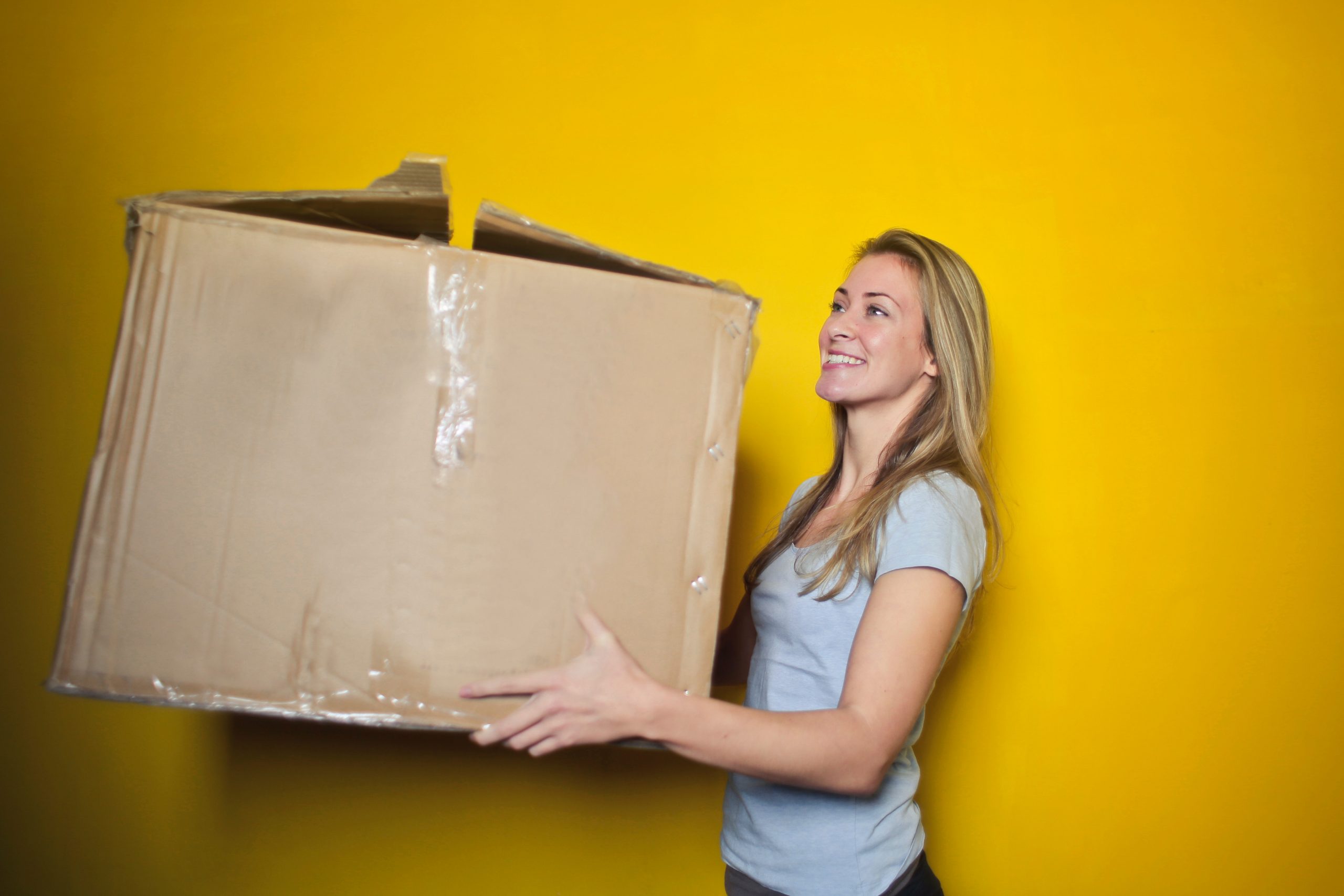 Full image of A woman carries a large cardboard box.