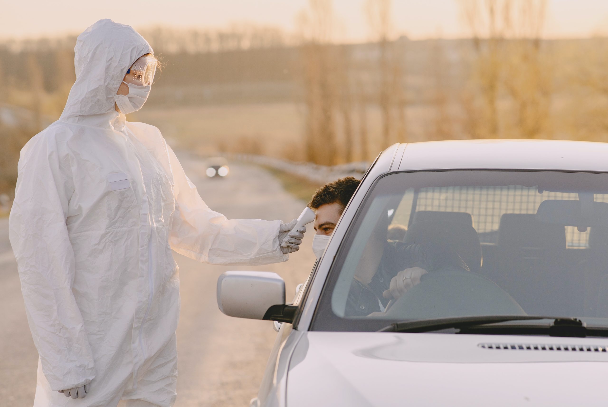 Full image of Driver's temperature being checked at the roadside by somebody in full protective equipment.
