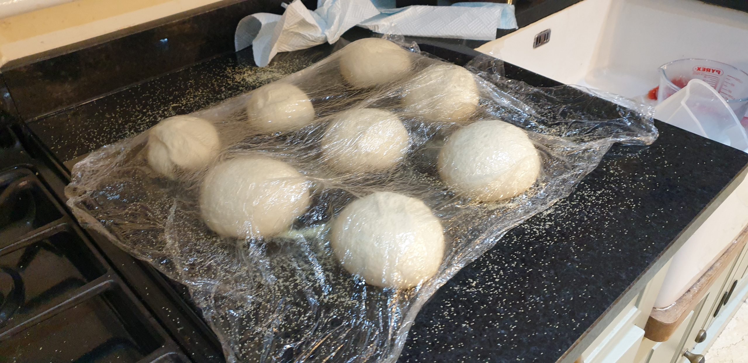 Full image of Pizza dough balls under cling film on a black marble surface.