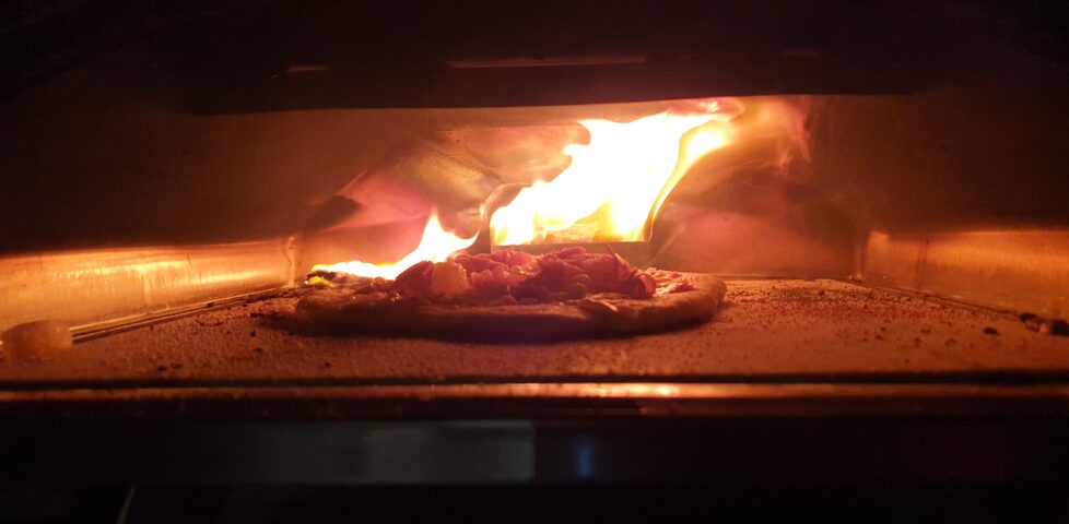 Pizza in an oven, fire raging behind and jumping onto the floor of the oven.