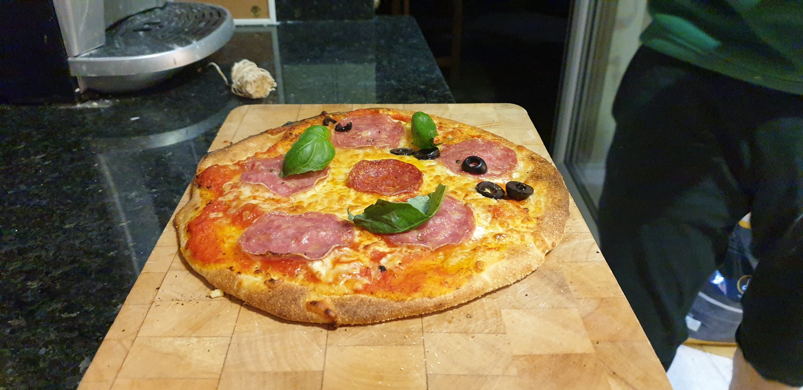 Full image of A salami and basil pizza with olives on half.