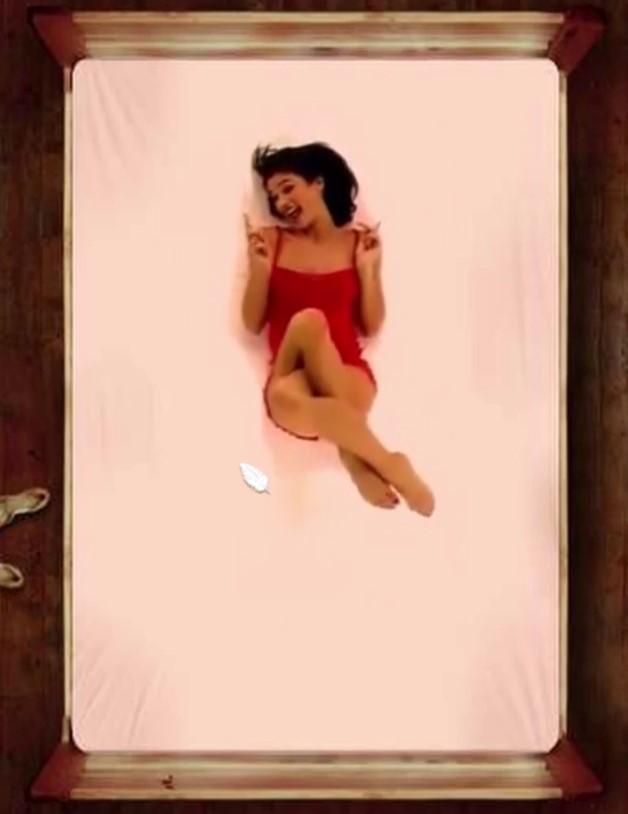 A woman lies on a bed with her legs crossed, playfully wagging her finger.