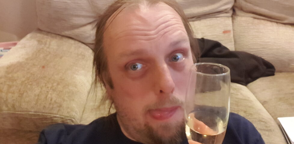 Dan with his tongue out holding a glass of champagne.