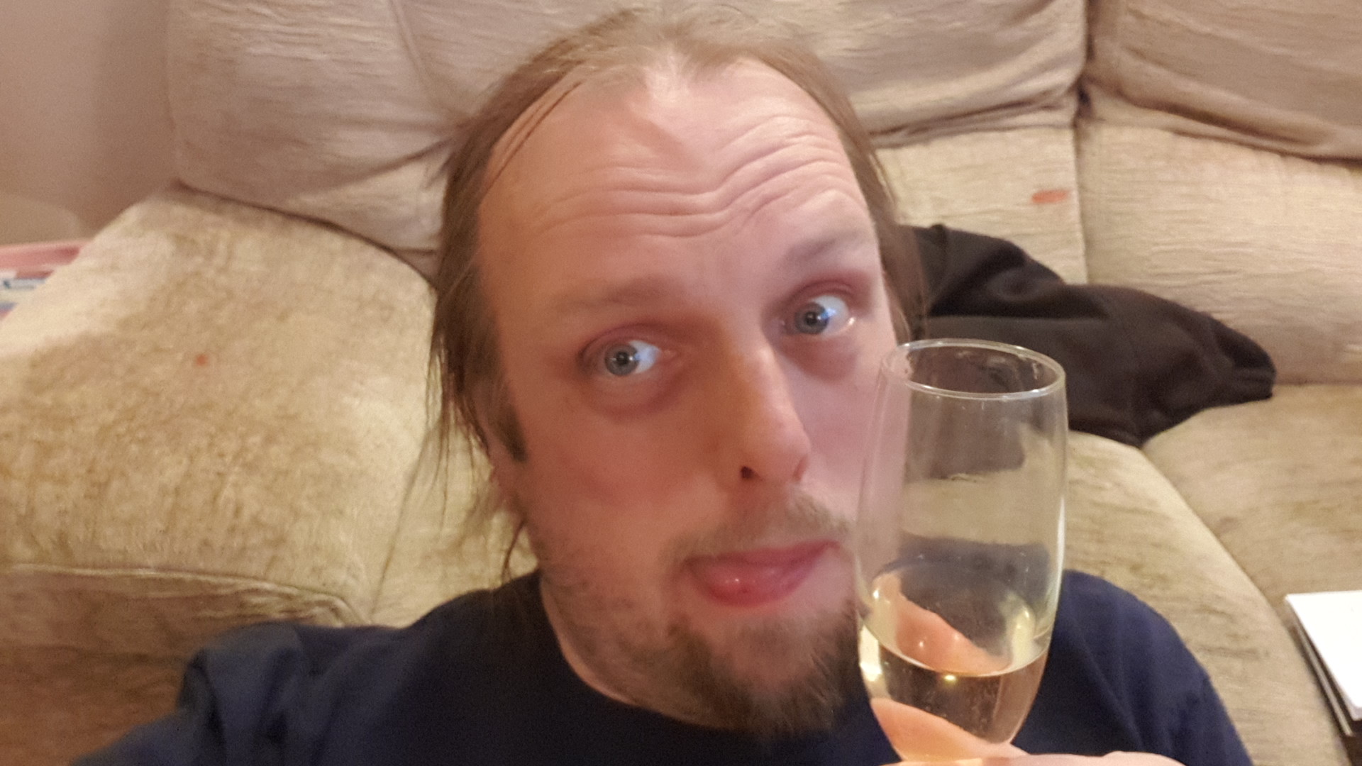 Full image of Dan with his tongue out holding a glass of champagne.