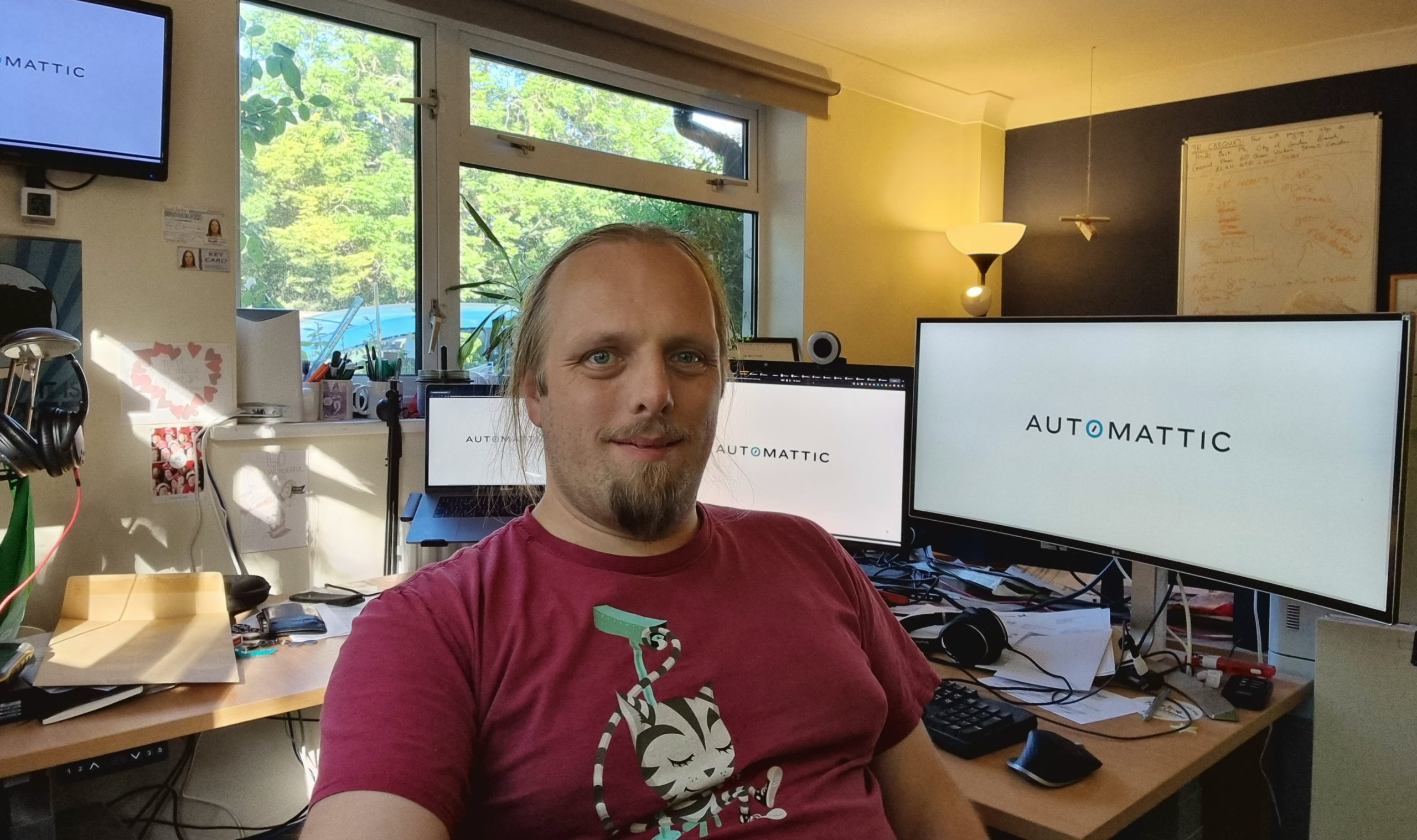 Full image of Dan sits in his office; behind him, four separate monitors show the Automattic logo.