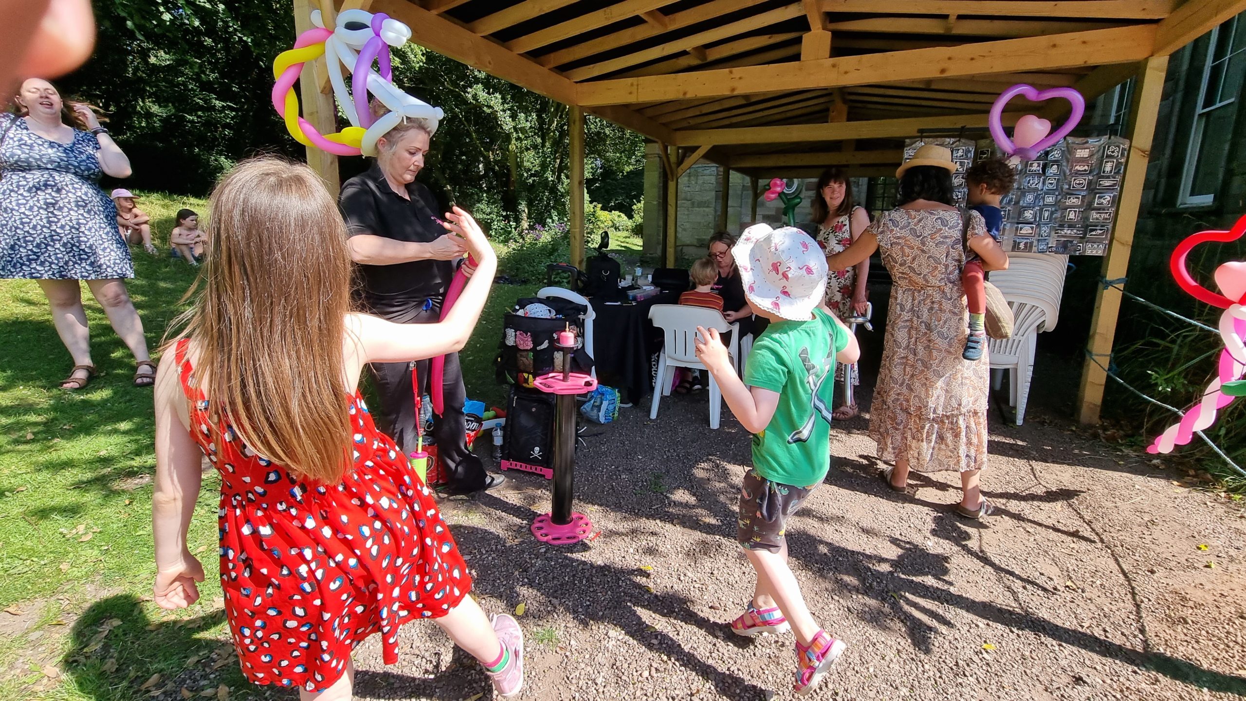 Full image of A balloon artist wearing a unicorn on her head makes sculptures for children.