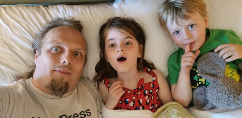 Dan and the kids in a bed at a hotel.