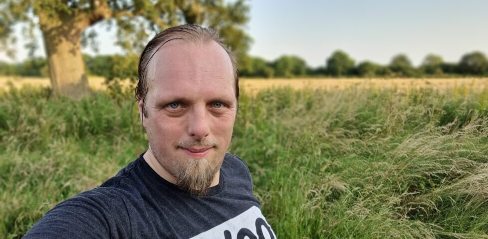 Selfie of Dan standing by a tree in a freshly-mowed cornfield.