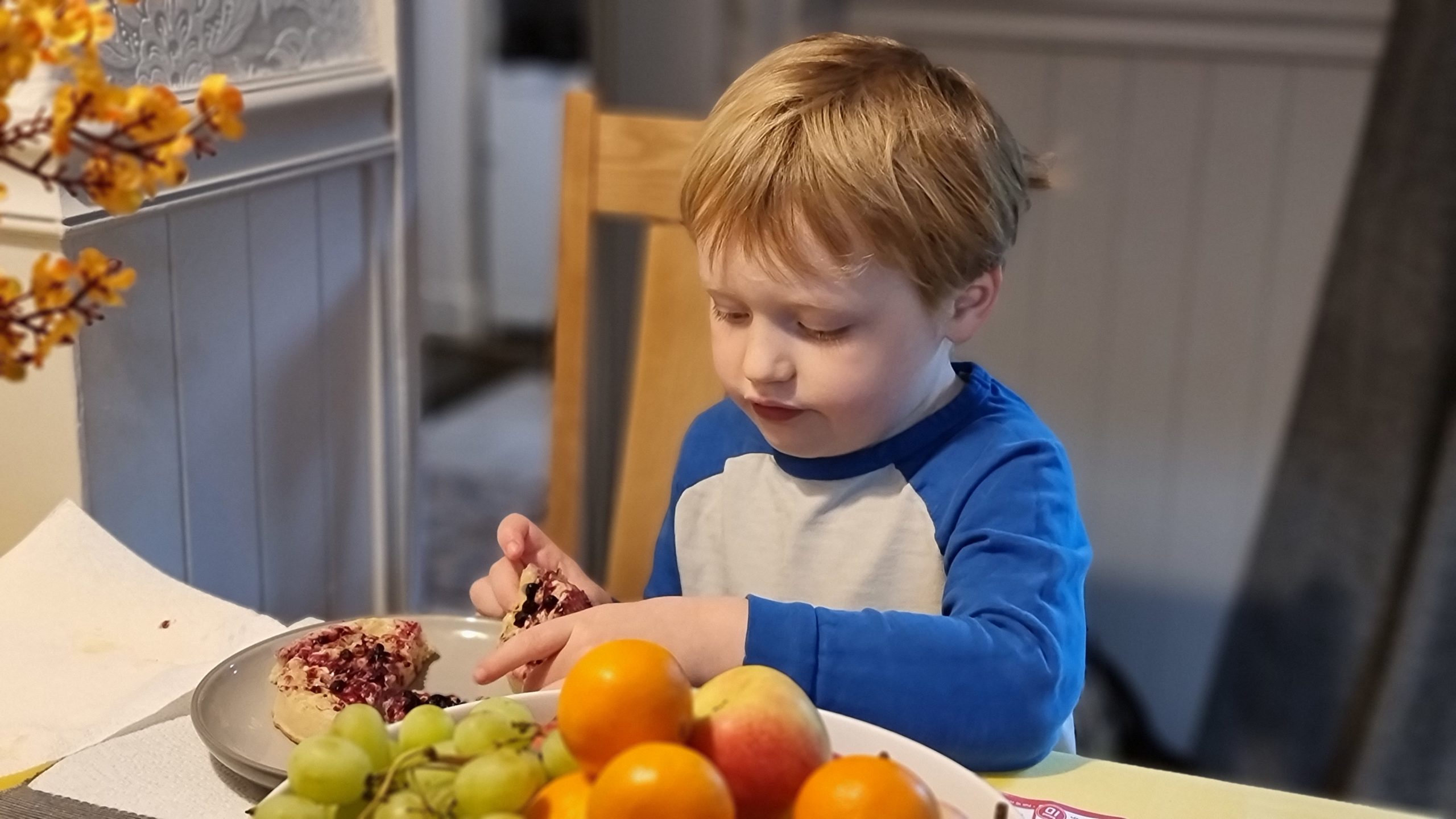 Full image of Boy eating a crumpet alongside a bowl of fruit.