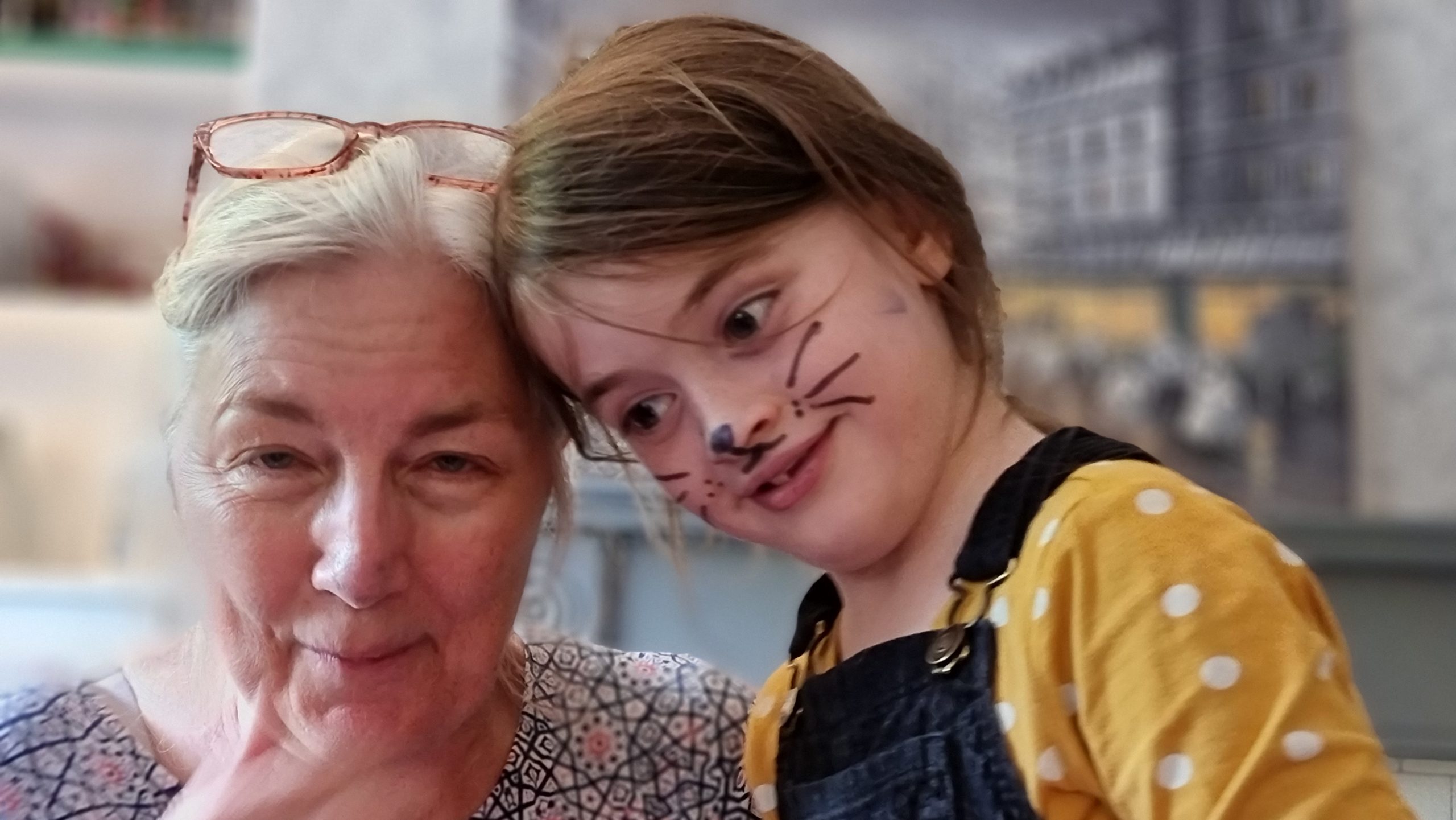 Full image of A woman and a girl; the girl is face-painted as a cat, the woman has bit of the face paint rubbed off onto her.