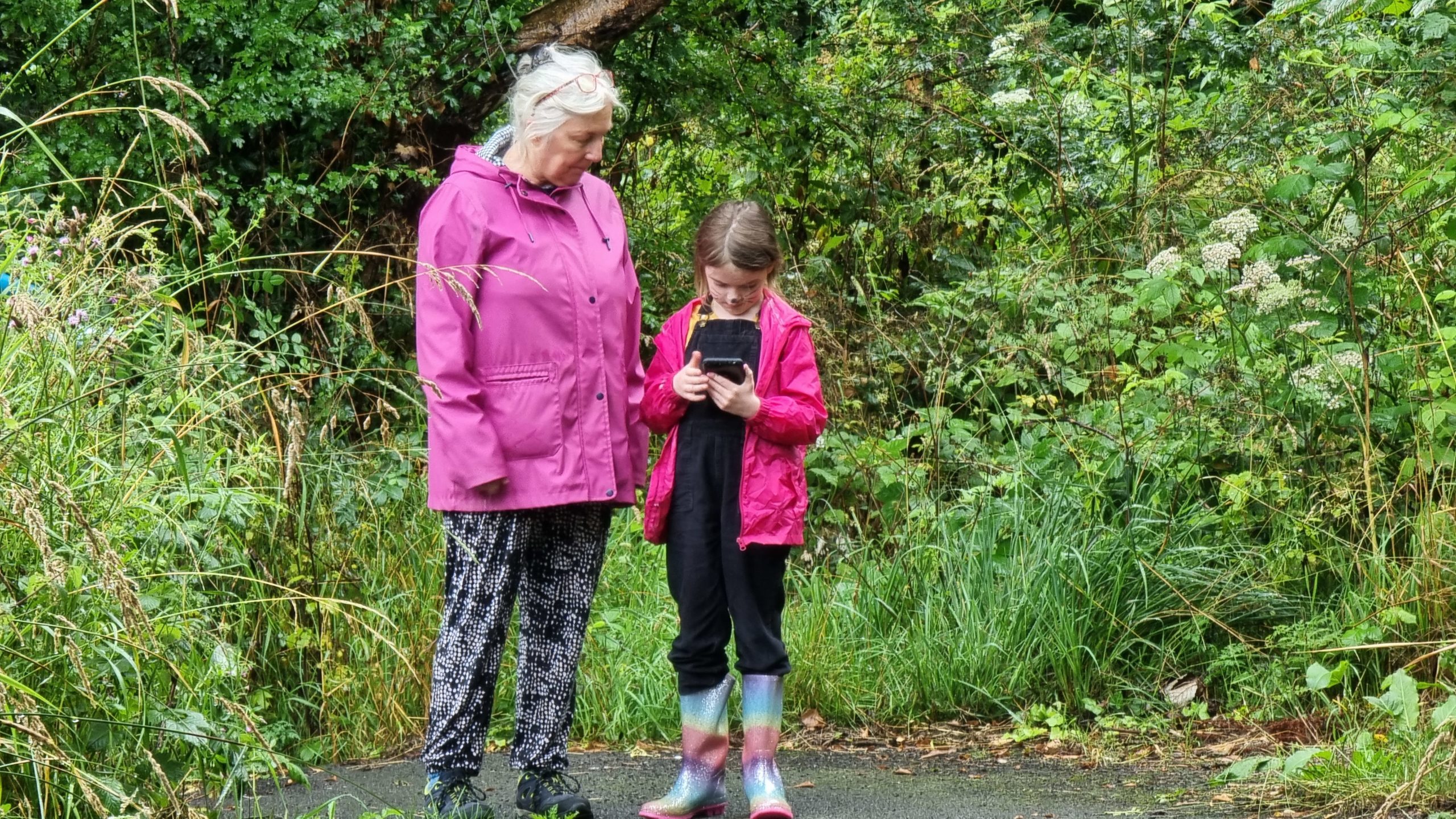 Full image of A woman and a girl outdoors looking at their mobile devices.
