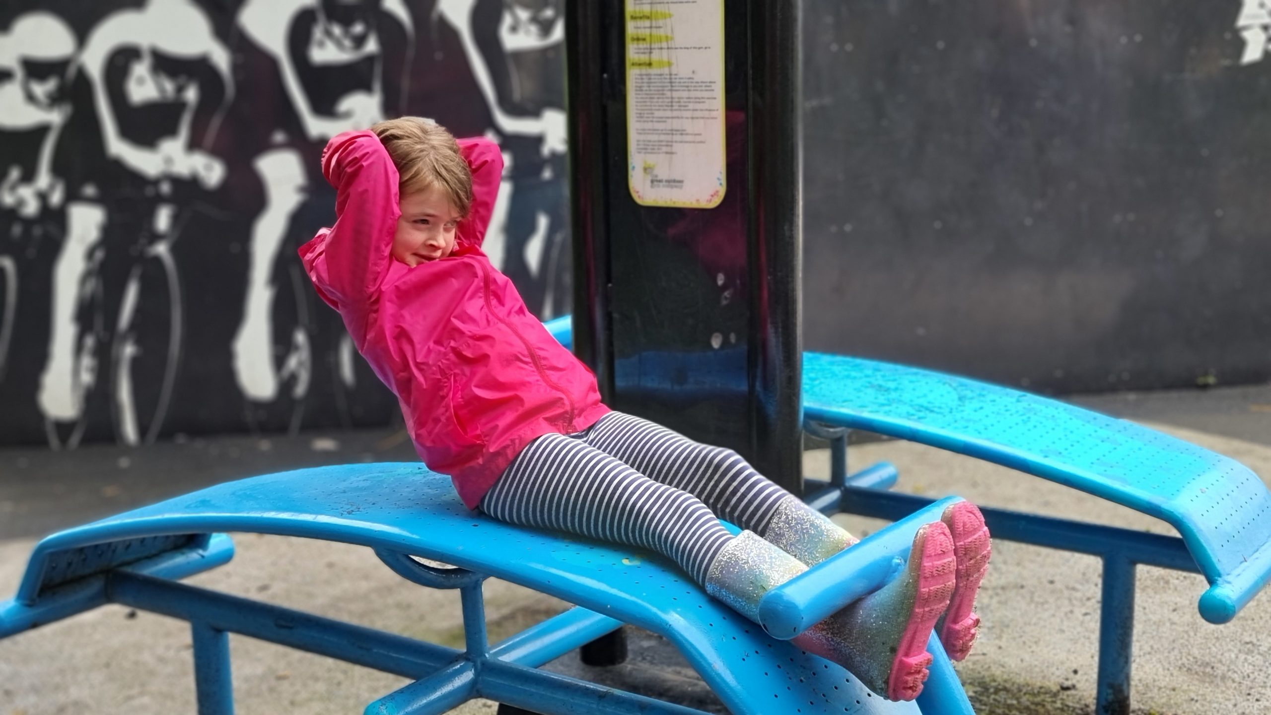 Full image of A girl does sit-ups in an outdoor gym.
