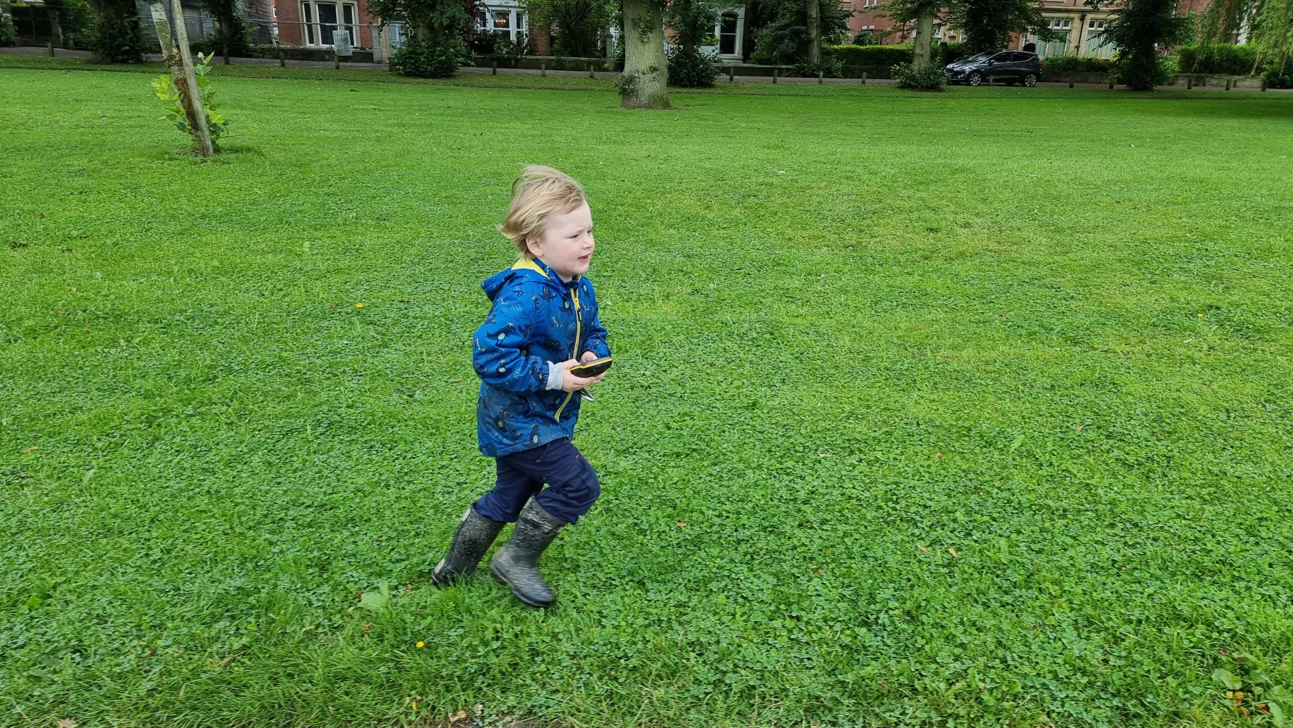 Full image of A boy, holding a GPS receiver, runs across a park lawn.