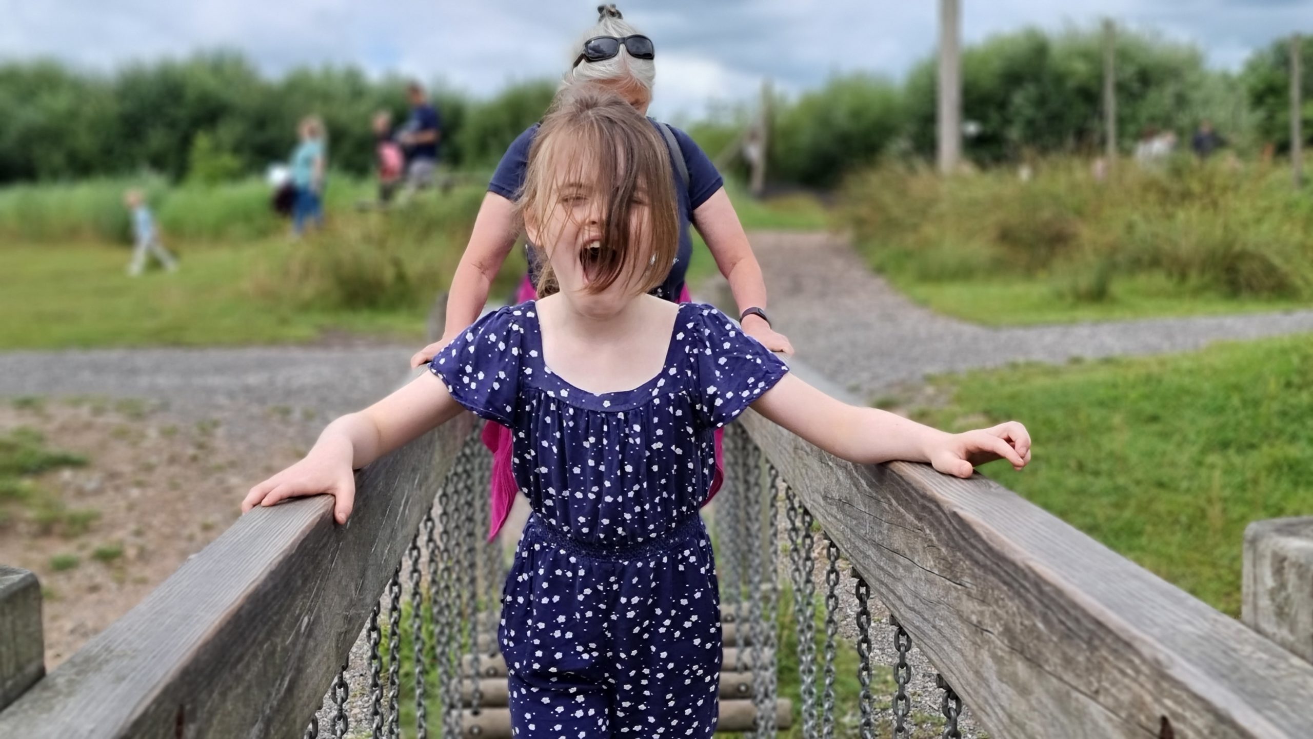 Full image of A girl shouts with excitement as she crosses a wobbly bridge.