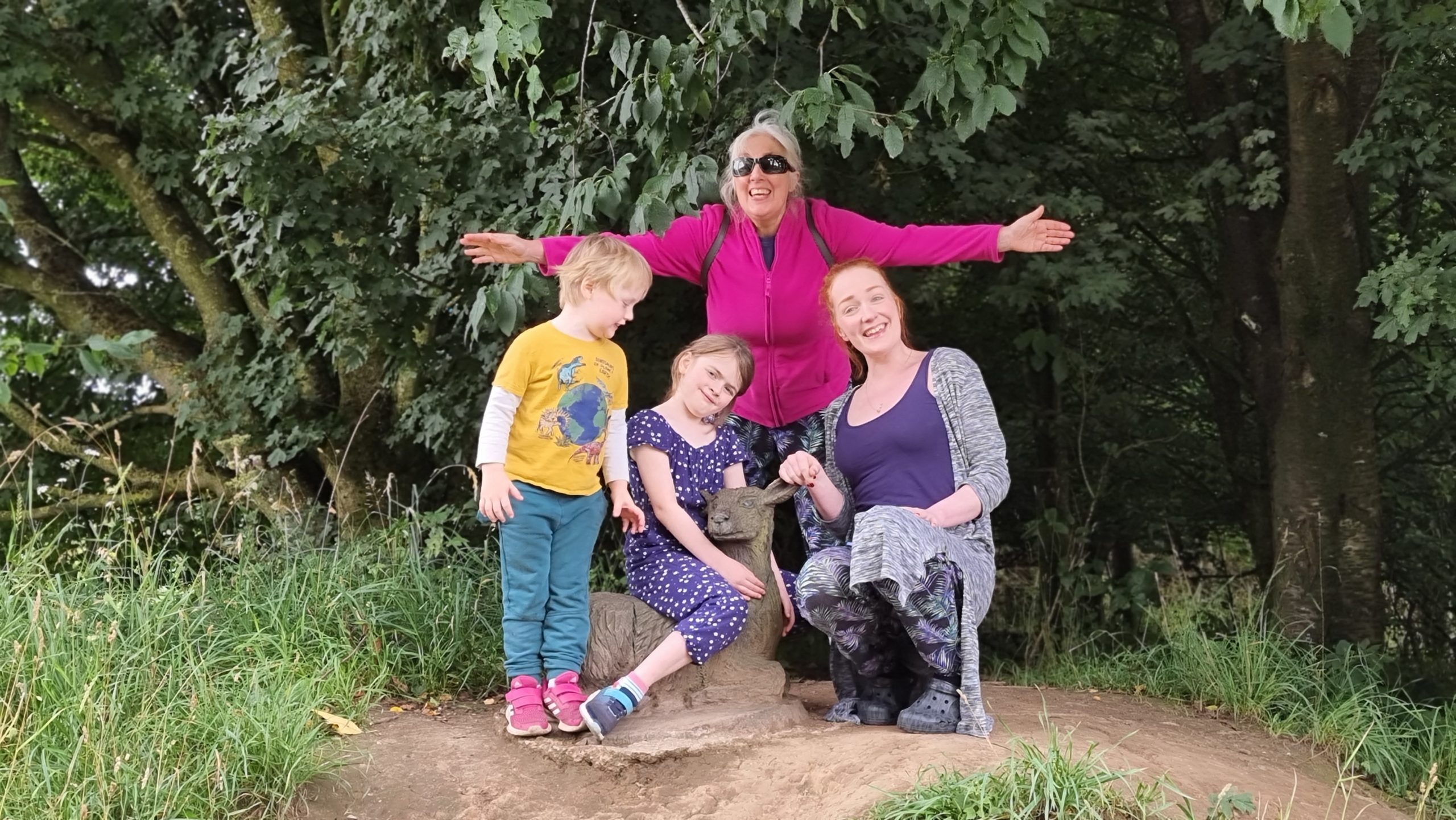 Full image of Two adults and two children pose with a wooden sculpture of a doe lying down.