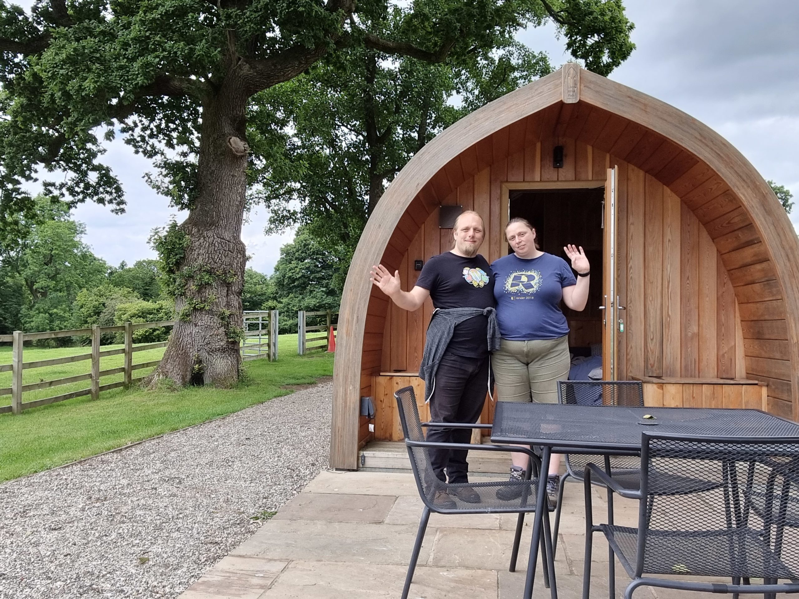 Full image of Dan and Ruth outside a wooden "pod" glamping structure.