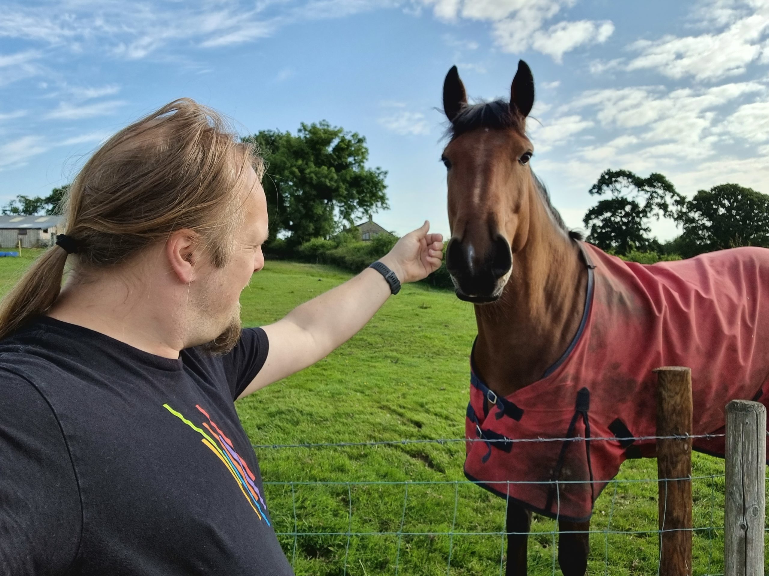 Full image of Dan strokes a large brown horse wearing a red jacket.