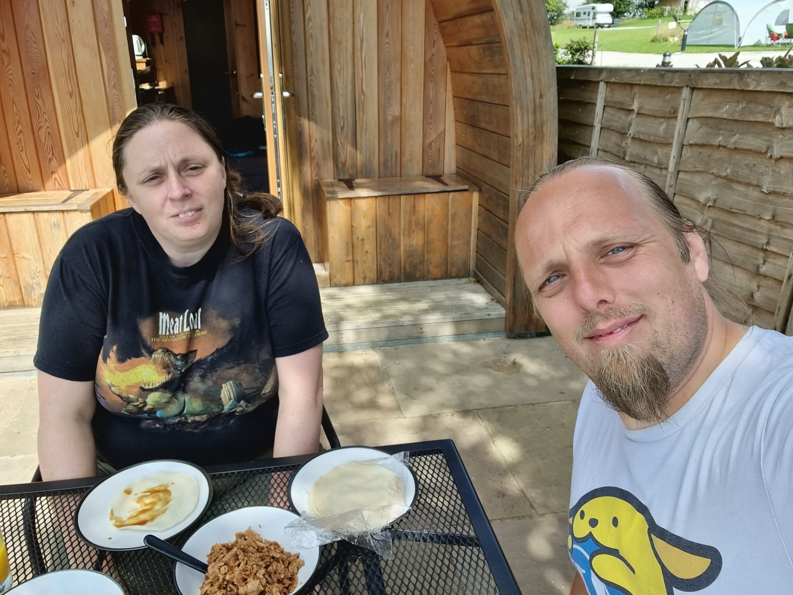 Full image of Ruth and Dan eat (fake) duck pancakes outside their lodge.
