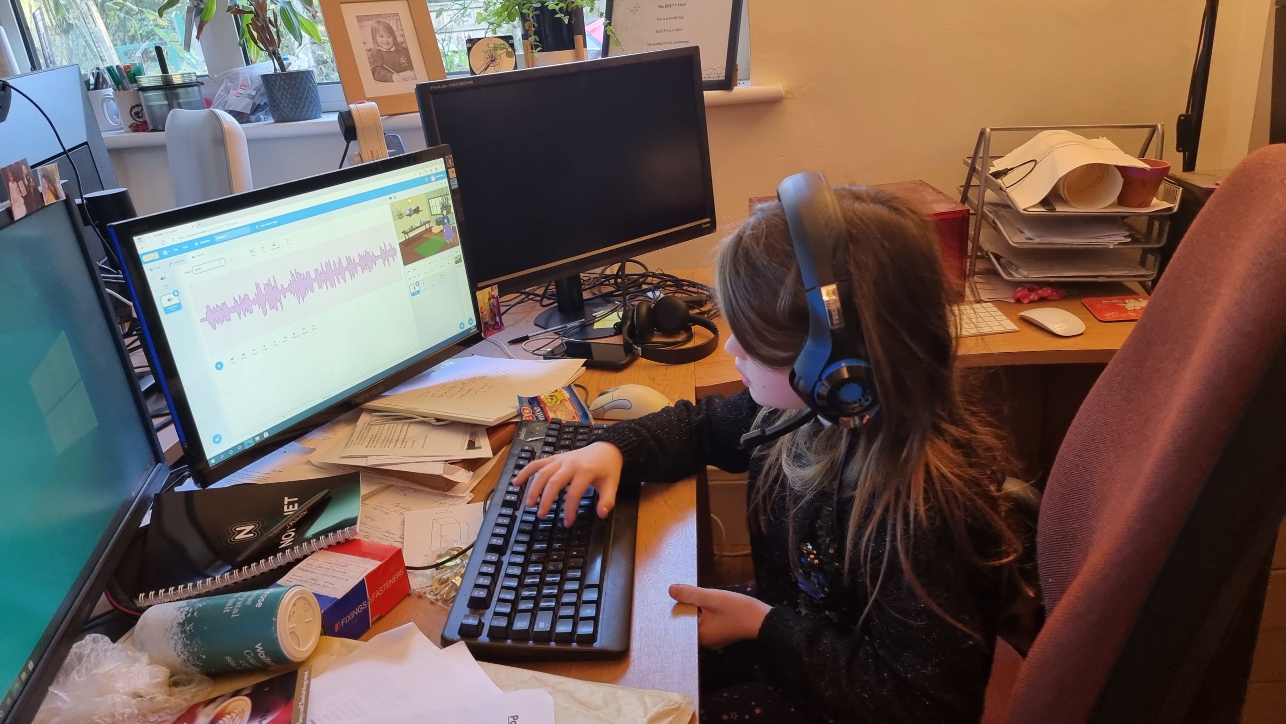 Full image of A girl wearing headphones programs in Scrach. On her screen a witch is hunting for a broomstick.