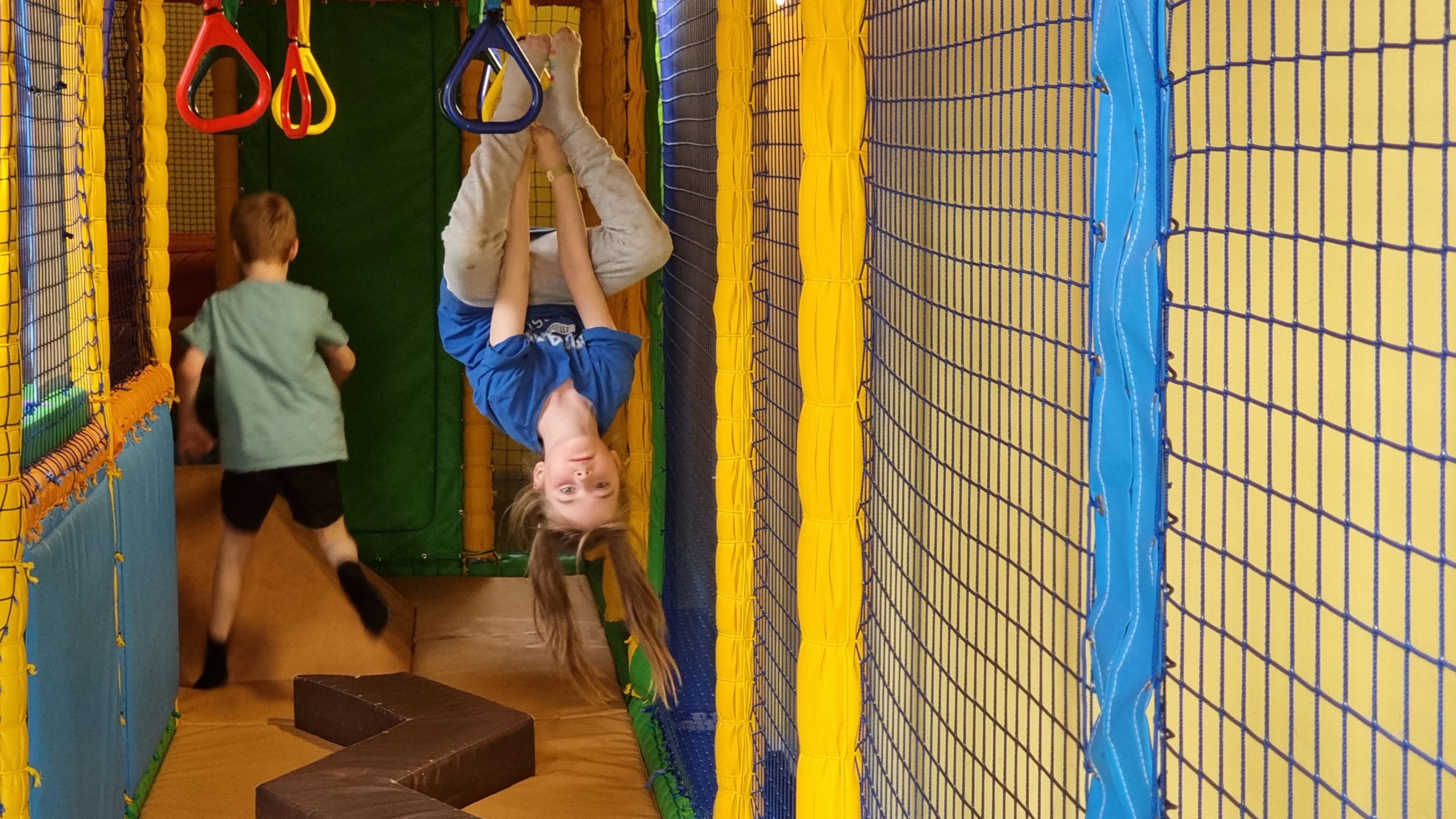 Full image of A girl hangs upside-down in a soft play area.