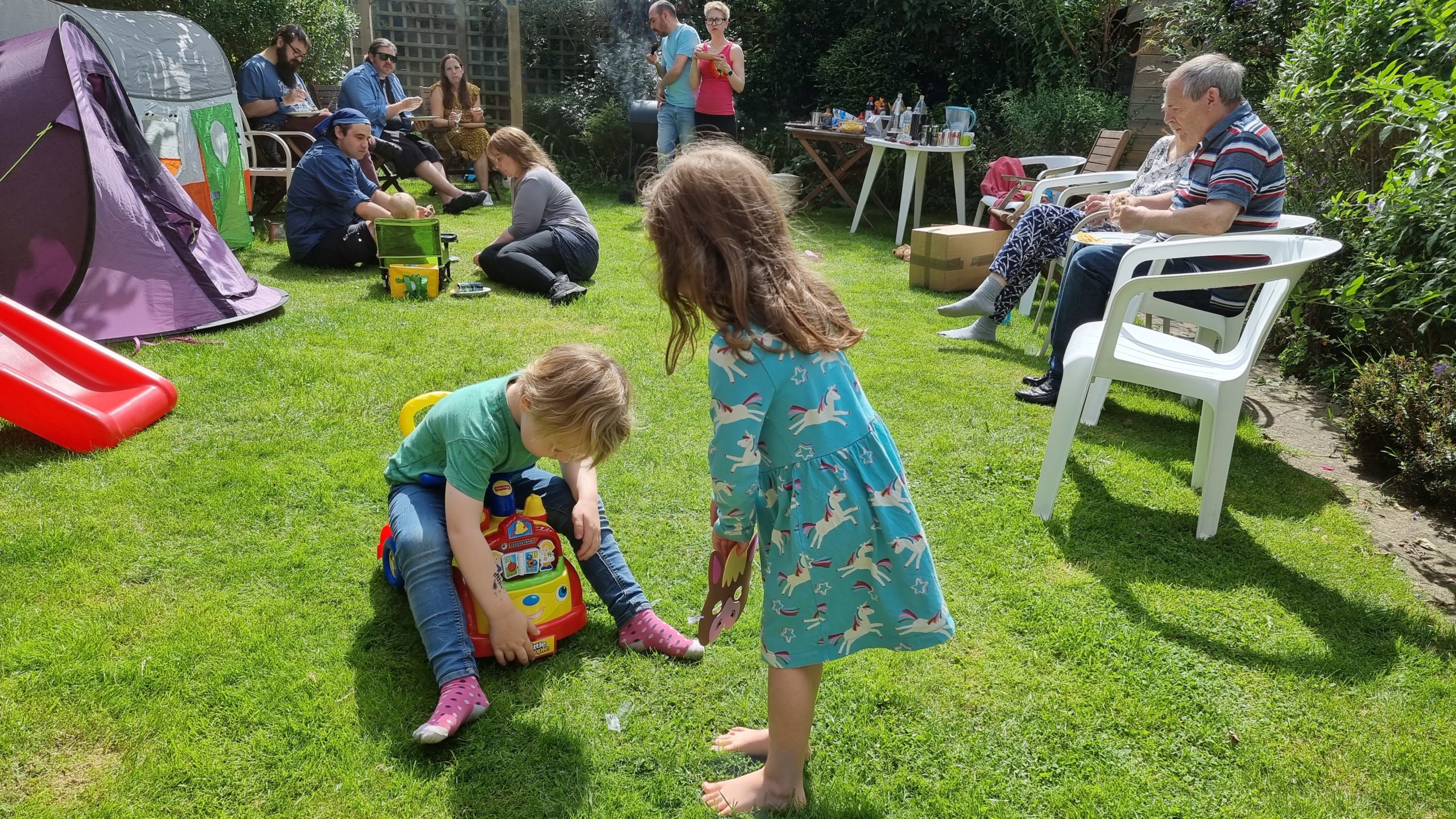 Full image of Children play together; adults sit and talk in the background.