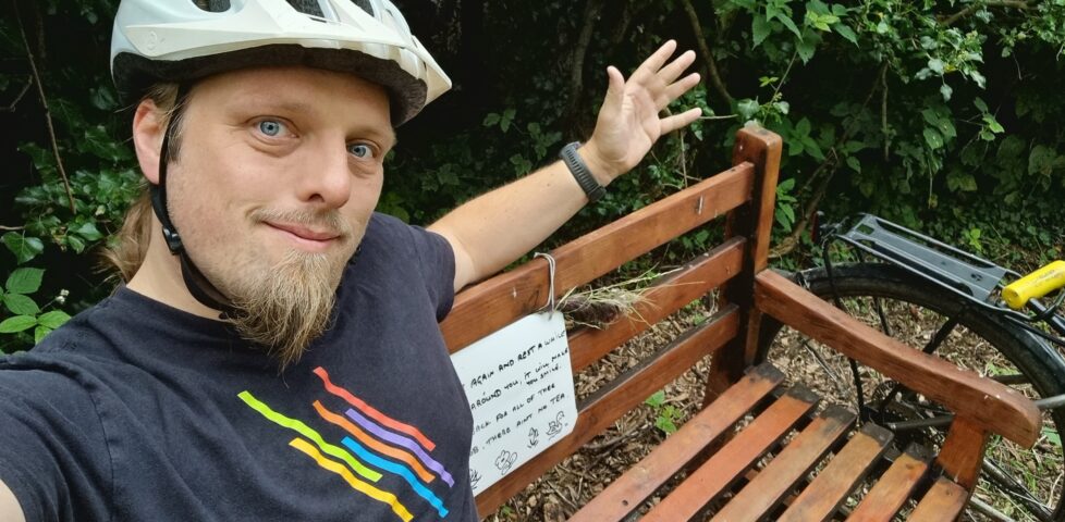 Dan wearing a cycle helmet sitting on a wooden bench.