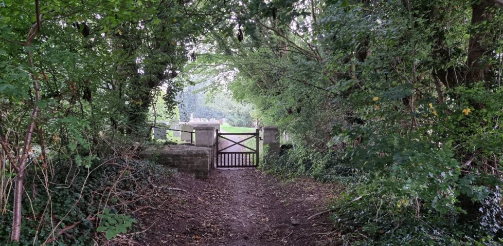 Churchyard gate at the end of a tree-lined path.