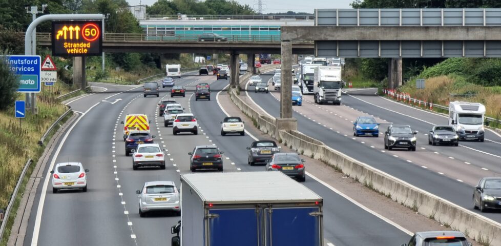 Motorway traffic moving past a 50 limit and "stranded vehicle" warning sign.
