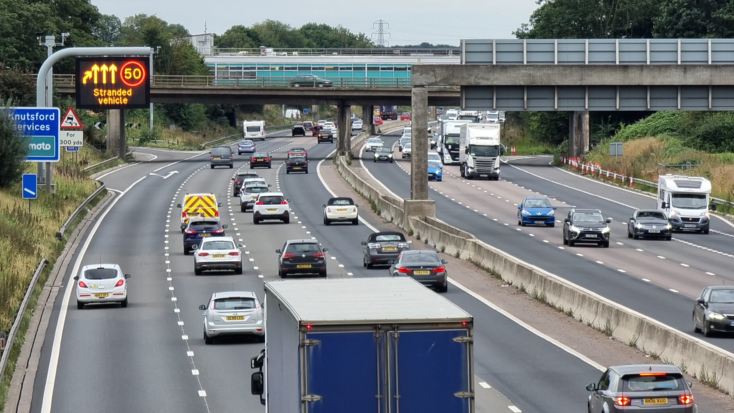 Full image of Motorway traffic moving past a 50 limit and "stranded vehicle" warning sign.