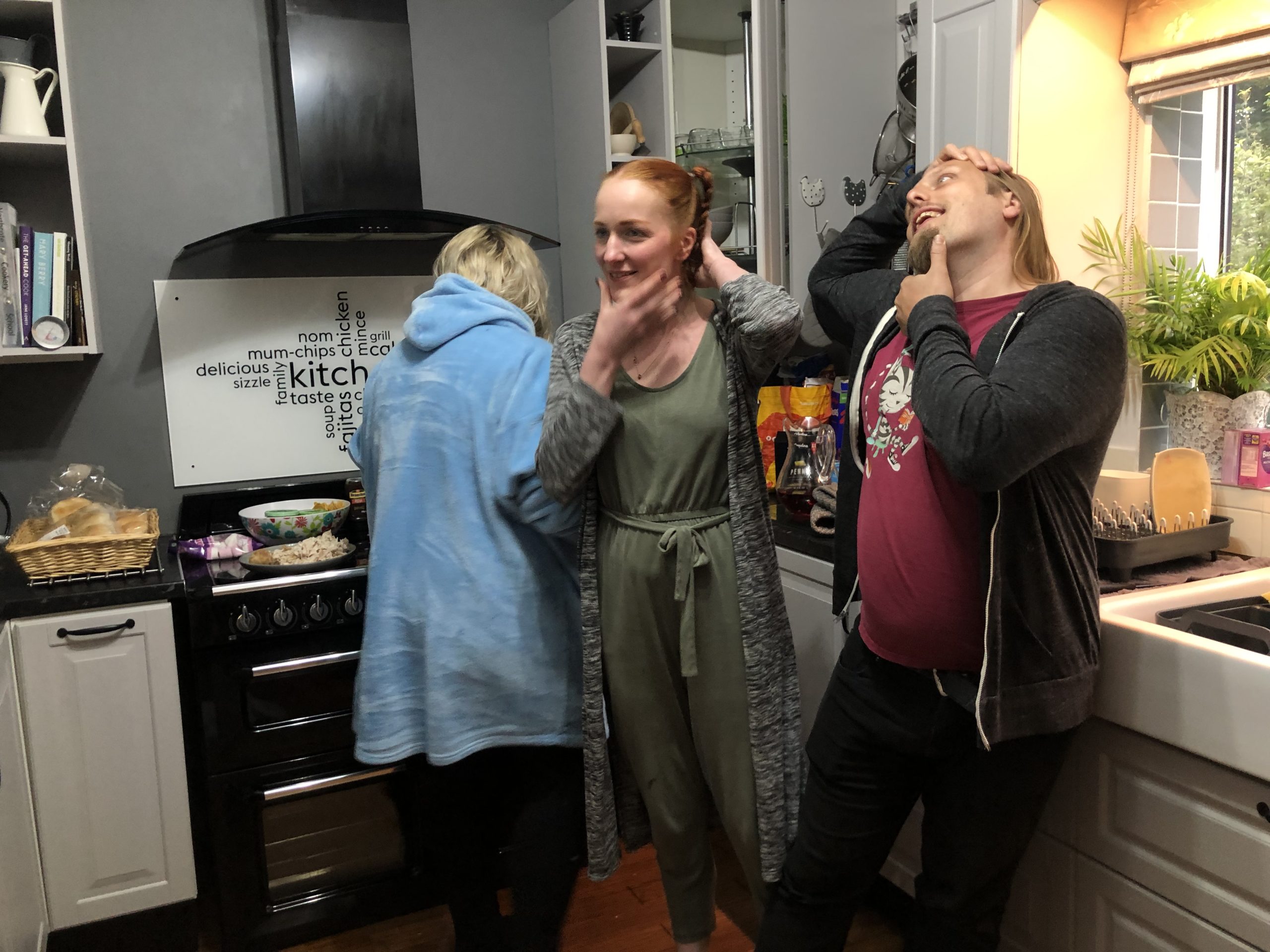 Full image of Dan and Sarah hold their heads with their hands, at a strange angle.