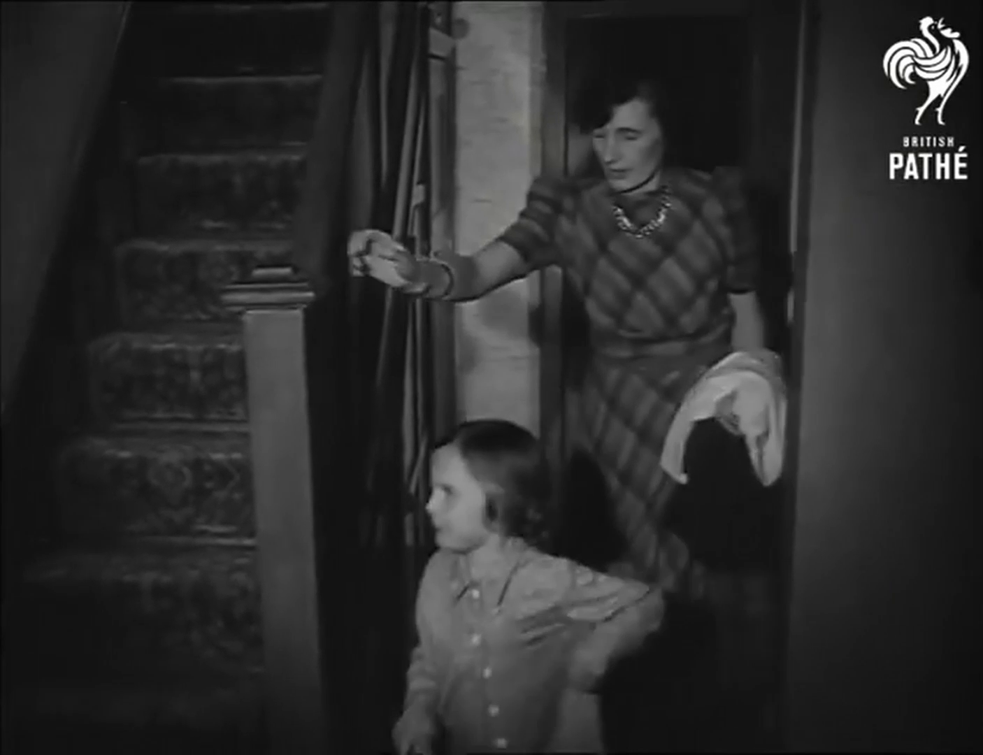 Full image of Black & white framegrab showing a woman following her child, wearing pyjamas, towards a staircase up.